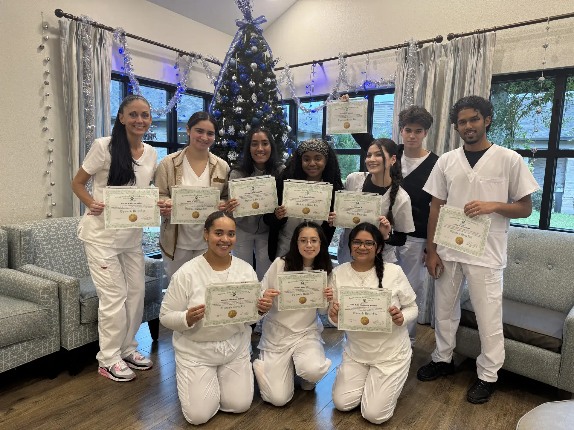 CNA training graduates holding nurse aide diplomas beside a Christmas tree